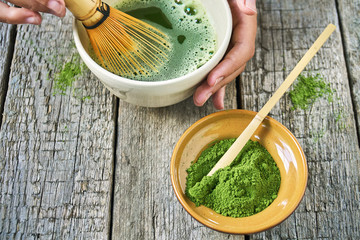 Matcha green tea accessoires on the rough wooden boards with girl's hands preparing matcha tea in a...