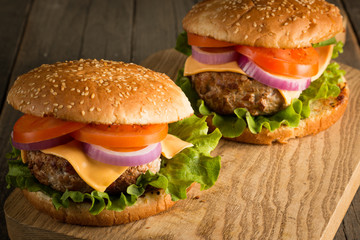 Home made hamburger with beef, onion, tomato, lettuce and cheese. Fresh burger close up on wooden rustic table with potato fries, beer and chips. Cheeseburger.