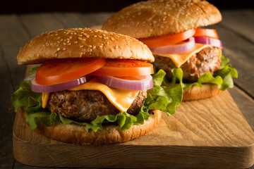 Home made hamburger with beef, onion, tomato, lettuce and cheese. Fresh burger close up on wooden rustic table with potato fries, beer and chips. Cheeseburger.
