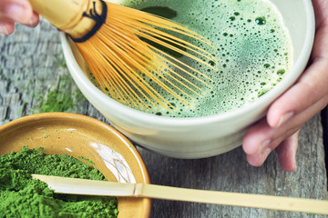 Matcha green tea accessoires on the rough wooden boards with girl's hands preparing matcha tea in a...