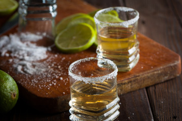 Macro photo of shots of gold Mexican tequila with lime and salt on wooden rustic background. Alcoholic drink concept. selective focus.