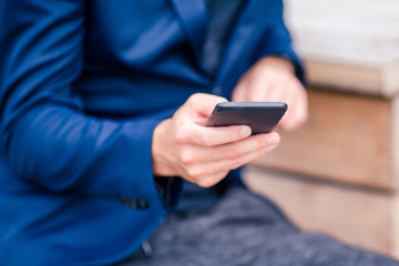Closeup of male hands is holding cellphone outdoors on the street. Man using mobile smartphone.