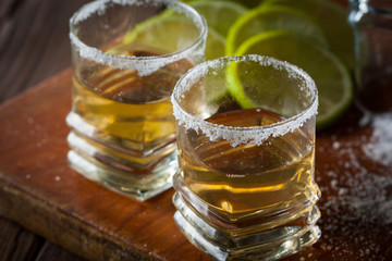 Macro photo of shots of gold Mexican tequila with lime and salt on wooden rustic background. Alcoholic drink concept. selective focus.