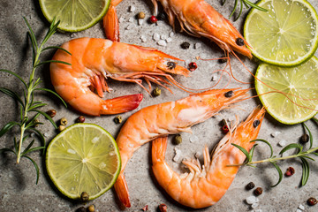 Tiger shrimps with lime, lemon, rosemary and black pepper spices on stone background. Fresh tasty prawns ready to be cooked.