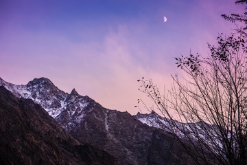 Landscape view of twilight sky with moon rise over snow capped mountains in Karakoram range. Passu village, upper Hunza. Gilgit Baltistan, Pakistan.