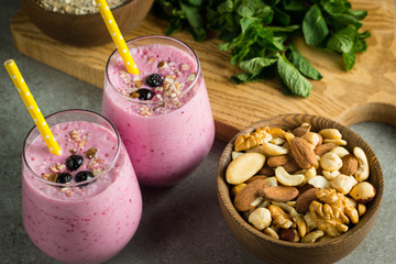 Glasses of berry smoothie with nuts, mint, blueberry, blackberry, raspberry, and yogurt on wooden table. Weight loss and diet concept. 