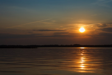 Sunset on the lake. Evening sky with beautiful clouds is reflected in the water of the lake