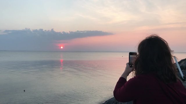Woman taking photograph of sunrise, sunset with phone