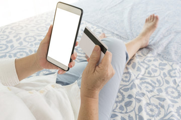 Woman using smart phone and credit card for paying bills or shopping online in the bedroom