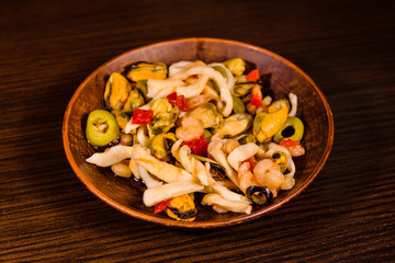 Ceramic plate with different sea food and olives on wooden table