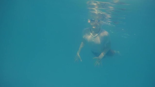 Cute small boy dives in blue pool in glasses on eyes. Underwater viewpoint of pool as boy dives and swims towards camera