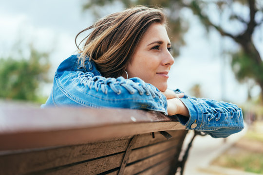 Young woman sitting on a bench daydreaming