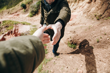 A hiker gives a hand to another person during hiking in a mountainous area. Support and teamwork.
