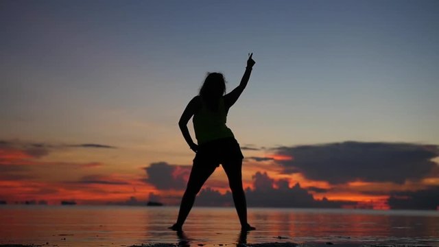 The smart girl enjoys the sunset, stands on the beach in the water and dances. slowmotion, HD, 1920x1080