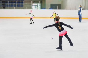 Little girl learning to ice skate. Figure skating school. Young figure skater practicing at indoor skating rink. - obrazy, fototapety, plakaty