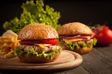 Home made hamburger with beef, onion, tomato, lettuce and cheese. Fresh burger close up on wooden rustic table with potato fries, beer and chips. Cheeseburger.