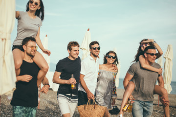 young men giving their girlfriends piggyback rides beach. Cheerful friends enjoying summertime on...