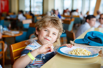 Cute healthy preschool kid boy eats pasta noodles sitting in school or nursery cafe. Happy child...