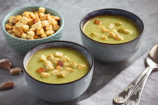 Broccoli cream soup with croutons on grey background.