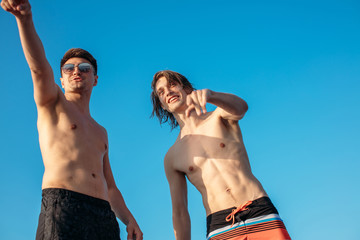Two happy caucasian male friends traveling on a yacht at open sea, sunbathing on the bow of the...