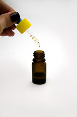 a drop of yellow liquid drains from a pipette with a yellow lid in a brown vial, isolate on a light background