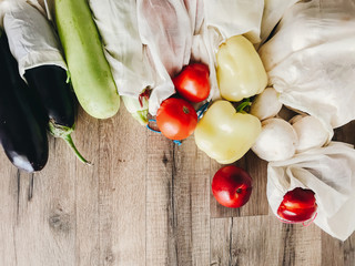 vegetables in eco cotton bags on table in the kitchen, zero waste shopping. flat lay. mushrooms, zucchini,eggplant, pepper, tomato, nectarines on wooden background.  ban plastic