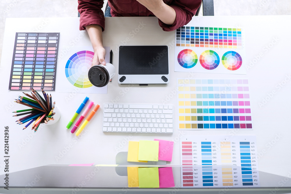 Poster Image of female creative graphic designer working on color selection and drawing on graphics tablet at workplace, top view workspace