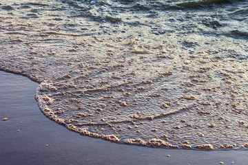 Waves on the sandy shore of a large river. The rays of light are reflected in the waves.