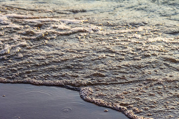 Waves on the sandy shore of a large river. The rays of light are reflected in the waves.