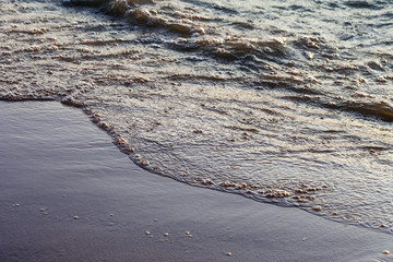 Waves on the sandy shore of a large river. The rays of light are reflected in the waves.