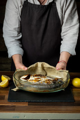 Chef cooking baked fish in glass pan on wooden table.