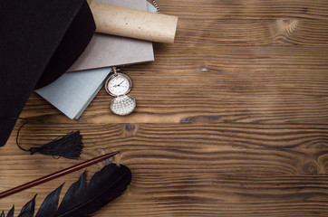 Graduate cap, pocket watch, stack of books, feather pen and scroll diploma on the wooden school...
