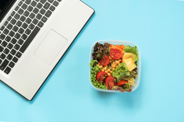 Healthy business lunch in the office, salad for snack on blue table. Top view with copy space. Concept proper nutrition. Take away lunchbox.