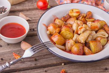 Traditional farmers food. Roasted red potatoes with carrots, onions and chicken breast pieces in old metal plate on wooden background. Served with red tomatoes and a mug of clean water. Tasty meal