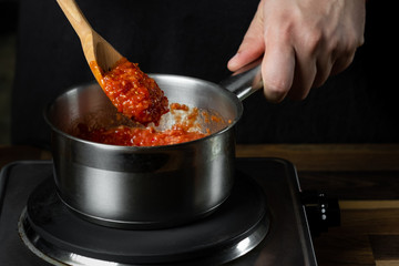 Cooking tomato sauce in metal saucepan by man cook hands, steps process on black background copy text recipe.