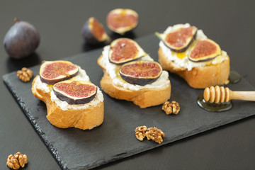 Ricotta sandwiches, fresh figs, walnuts and honey on a slate plate on a black background