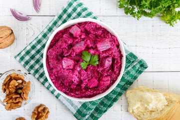 Delicious salad with boiled beets, herring, nuts, onions in a white ceramic bowl. Top view.
