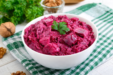 Delicious salad with boiled beets, herring, nuts, onions in a white ceramic bowl.