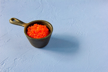 Small iron pot full of red salmon caviar at blue vintage background