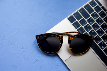 Stylish modern ladie's stuff: golden laptop and fashionable sunglasses at blue vintage background