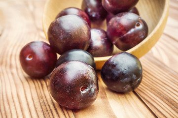 Plums scattered from wooden bowl on the table.
