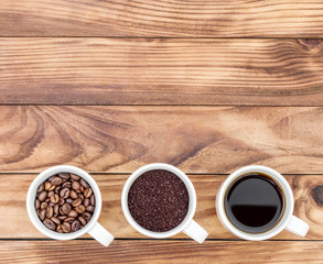 Cups with coffee drink, ground coffee and beans on wooden background. Top view. Space for text.