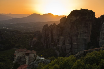 Huge rocks with monasteries and sunset behind distant mountains in Meteora, Thessaly, Greece
