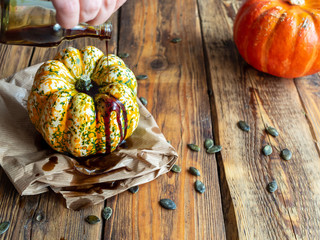 Frauenhand mit Kürbiskernöl in einer Glasflasche und ein Kürbis auf einem braunen Holztisch
