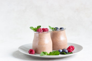 Chocolate dessert (panna cotta, mousse or pudding) in portion glass jars with raspberries, blueberries and mint on light grey background