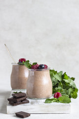 Chocolate dessert (panna cotta, mousse or pudding) in portion glass jars with raspberries, blueberries and mint on light grey background