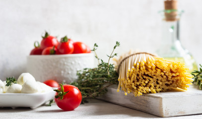 Ingredients for cooking pasta. Spaghetti, cherry tomatoes, thyme, rosemary, olive oil and mozzarella on light grey background. Italian pasta ingredients.