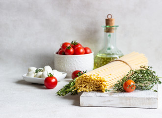 Ingredients for cooking pasta. Spaghetti, cherry tomatoes, thyme, rosemary, olive oil and mozzarella on light grey background. Italian pasta ingredients.