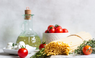 Ingredients for cooking pasta. Spaghetti, cherry tomatoes, thyme, rosemary, olive oil and mozzarella on light grey background. Italian pasta ingredients.