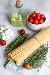 Ingredients for cooking pasta. Spaghetti, cherry tomatoes, thyme, rosemary, olive oil and mozzarella on light grey background. Italian pasta ingredients.